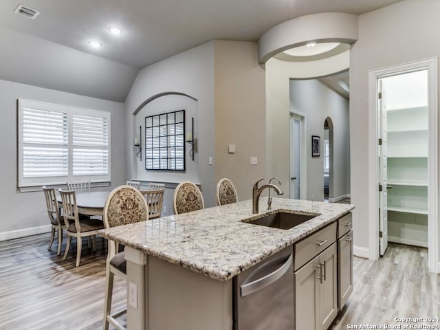 kitchen with dishwasher, sink, vaulted ceiling, an island with sink, and light stone counters