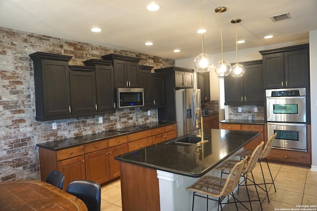 kitchen featuring appliances with stainless steel finishes, light tile patterned floors, pendant lighting, a center island with sink, and a breakfast bar area