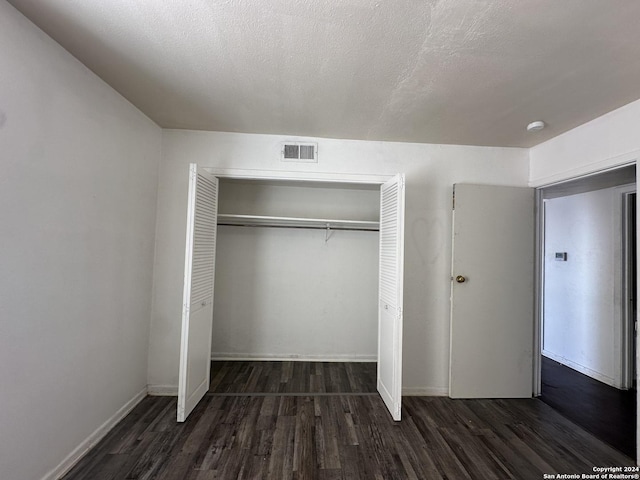 unfurnished bedroom with a textured ceiling, a closet, and dark hardwood / wood-style floors