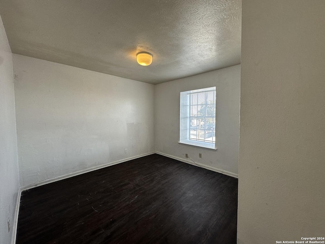 spare room featuring a textured ceiling and dark hardwood / wood-style floors