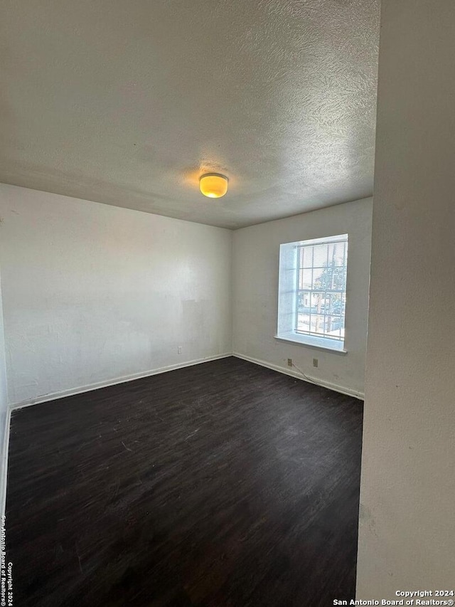 empty room with a textured ceiling and dark wood-type flooring