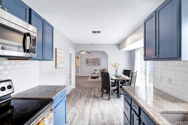 kitchen featuring ceiling fan, blue cabinetry, tasteful backsplash, light hardwood / wood-style floors, and stainless steel appliances