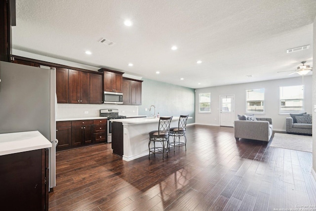 kitchen with stainless steel appliances, a center island with sink, dark hardwood / wood-style floors, and a healthy amount of sunlight