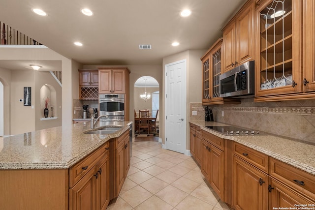 kitchen with appliances with stainless steel finishes, tasteful backsplash, an island with sink, sink, and light tile patterned floors