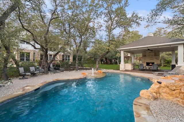 view of pool with ceiling fan, a gazebo, an outdoor stone fireplace, and a patio