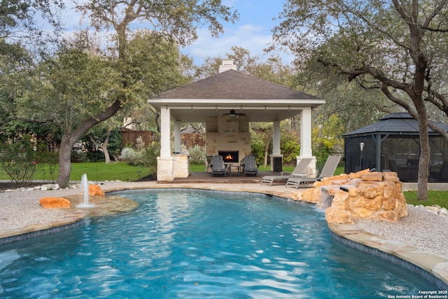 view of pool with ceiling fan, a gazebo, pool water feature, and exterior fireplace