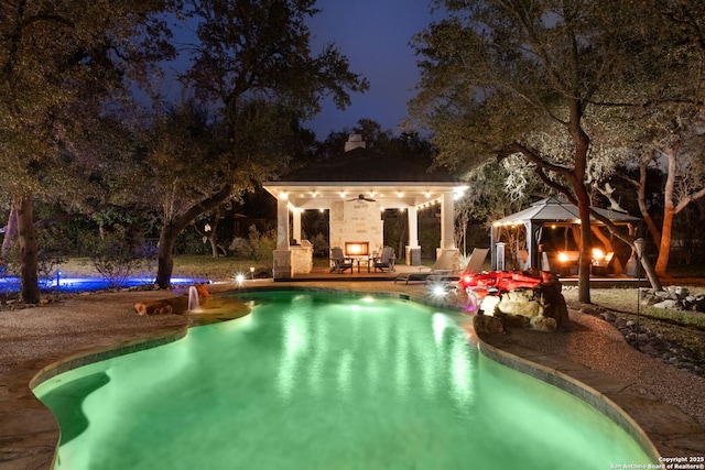 pool at twilight featuring a gazebo, an outdoor fireplace, and a patio