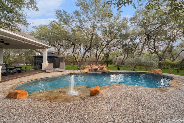 view of swimming pool with ceiling fan, a patio area, a gazebo, and pool water feature