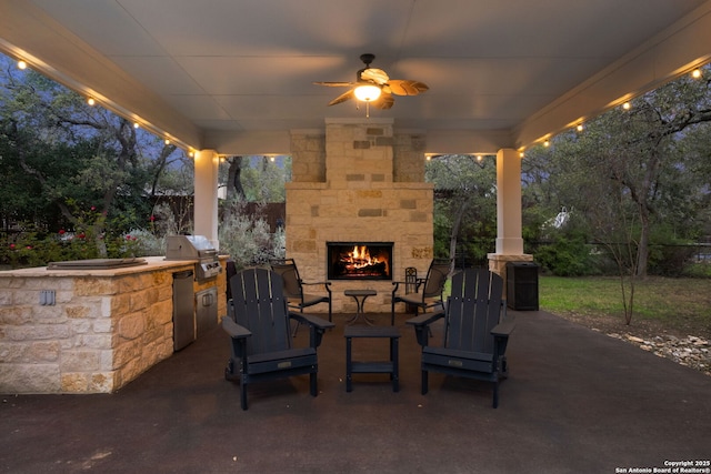 view of patio / terrace featuring ceiling fan, exterior kitchen, an outdoor stone fireplace, and a grill