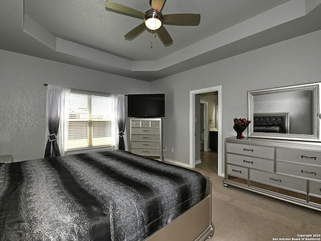 carpeted bedroom with a tray ceiling, ensuite bath, and ceiling fan