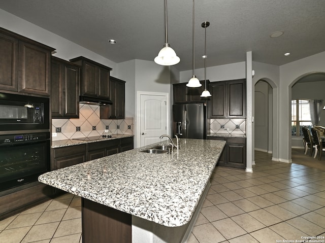 kitchen with sink, hanging light fixtures, an island with sink, dark brown cabinets, and black appliances