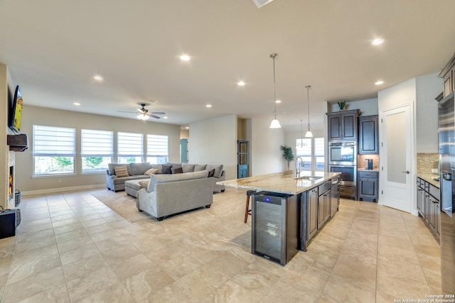 kitchen featuring pendant lighting, a breakfast bar, a center island with sink, sink, and beverage cooler