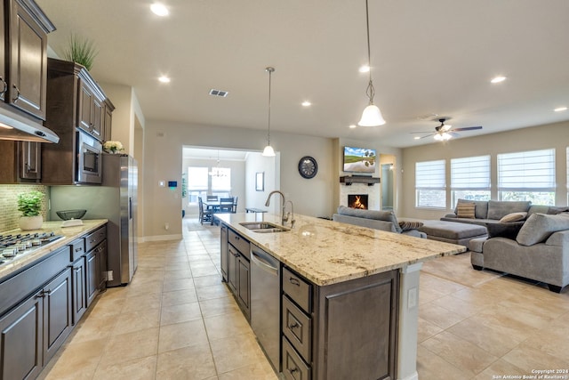 kitchen with dark brown cabinets, stainless steel appliances, sink, decorative light fixtures, and an island with sink