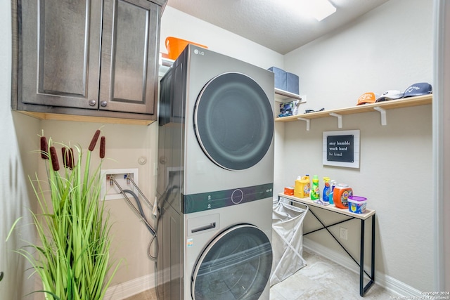 clothes washing area featuring stacked washer / drying machine and cabinets