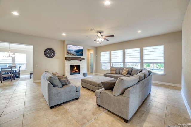 tiled living room featuring ceiling fan with notable chandelier and a stone fireplace