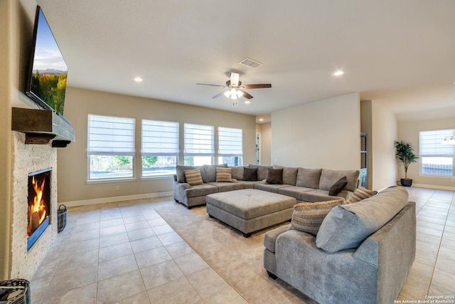 tiled living room featuring a stone fireplace and ceiling fan