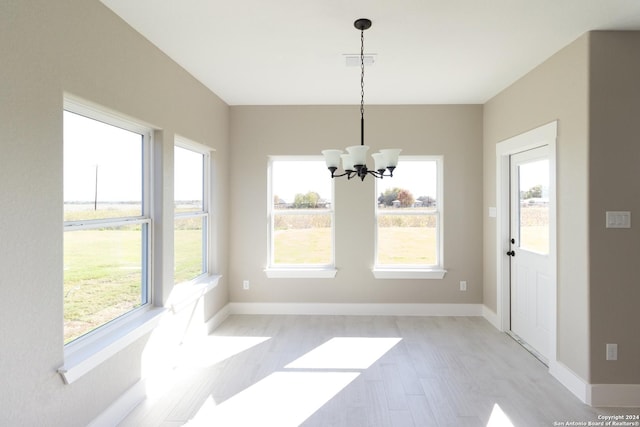 unfurnished dining area featuring plenty of natural light, light hardwood / wood-style floors, and a chandelier