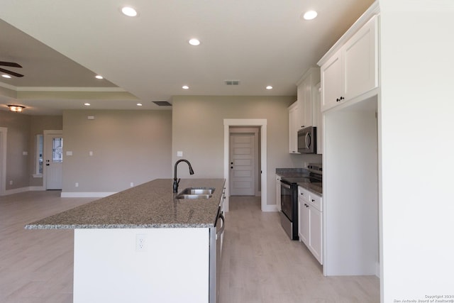 kitchen featuring black electric range, white cabinetry, a kitchen island with sink, and sink