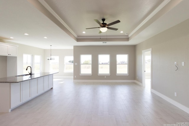 kitchen with a tray ceiling, a healthy amount of sunlight, sink, dark stone countertops, and white cabinets