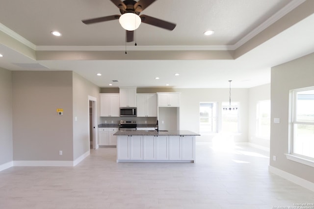 kitchen featuring dark stone counters, white cabinets, a center island with sink, ornamental molding, and appliances with stainless steel finishes