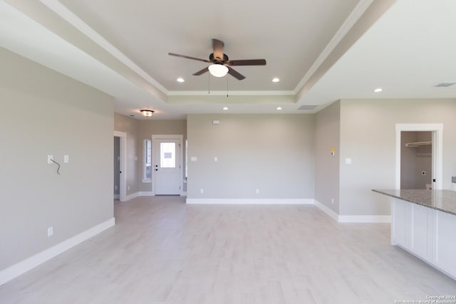 unfurnished living room featuring a raised ceiling, ceiling fan, light hardwood / wood-style flooring, and crown molding