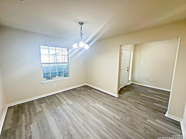 unfurnished dining area with a chandelier, a textured ceiling, and dark hardwood / wood-style floors