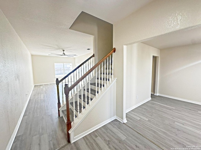 stairs with hardwood / wood-style floors, ceiling fan, and a textured ceiling