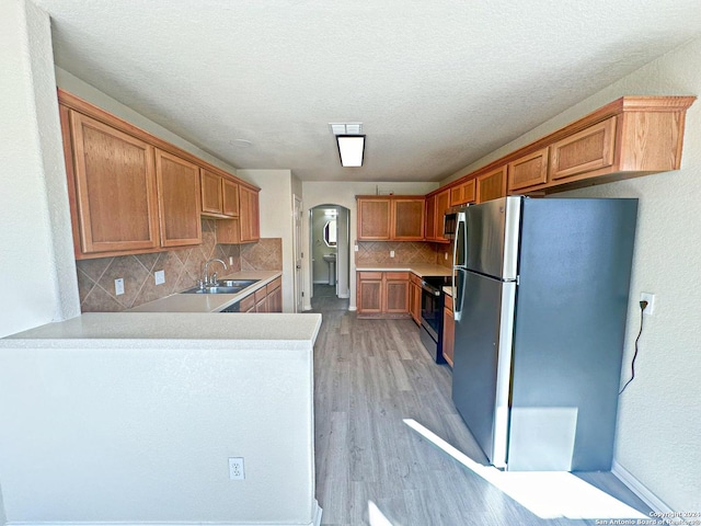 kitchen with decorative backsplash, a textured ceiling, appliances with stainless steel finishes, light hardwood / wood-style floors, and kitchen peninsula