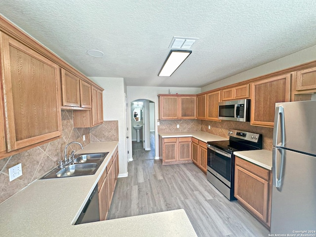 kitchen with sink, light hardwood / wood-style flooring, backsplash, a textured ceiling, and appliances with stainless steel finishes