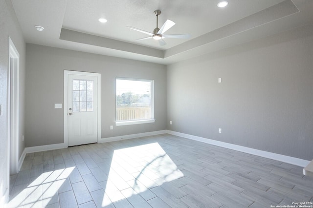 empty room with a raised ceiling, ceiling fan, and light wood-type flooring