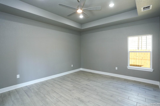 unfurnished room with a tray ceiling, ceiling fan, and light hardwood / wood-style flooring