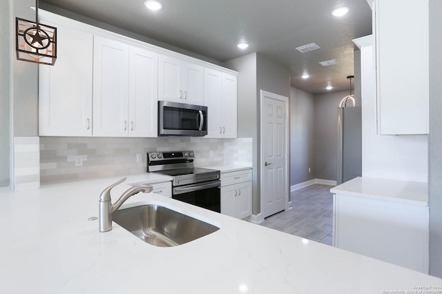 kitchen featuring sink, hanging light fixtures, stainless steel appliances, backsplash, and white cabinets