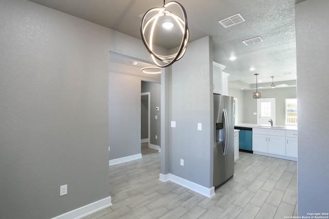 kitchen with white cabinets, sink, hanging light fixtures, light wood-type flooring, and stainless steel appliances