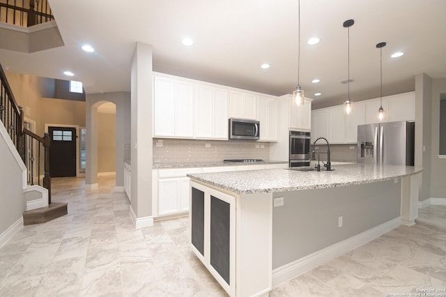 kitchen with sink, an island with sink, decorative backsplash, white cabinets, and appliances with stainless steel finishes