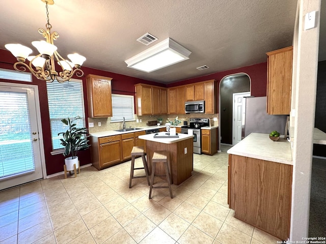 kitchen with a kitchen bar, appliances with stainless steel finishes, pendant lighting, a chandelier, and a kitchen island