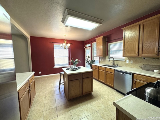 kitchen with a wealth of natural light, stainless steel appliances, sink, decorative light fixtures, and a kitchen island