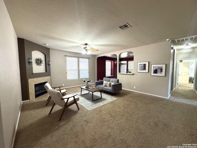 carpeted living room with ceiling fan, a fireplace, and a textured ceiling