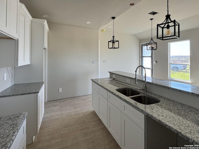 kitchen with light wood-type flooring, light stone counters, sink, pendant lighting, and white cabinets