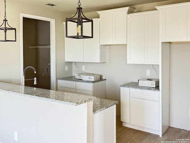 kitchen with light stone countertops, light wood-type flooring, pendant lighting, white cabinets, and a chandelier