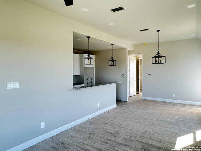 kitchen with white cabinets, hanging light fixtures, stone countertops, and light hardwood / wood-style floors