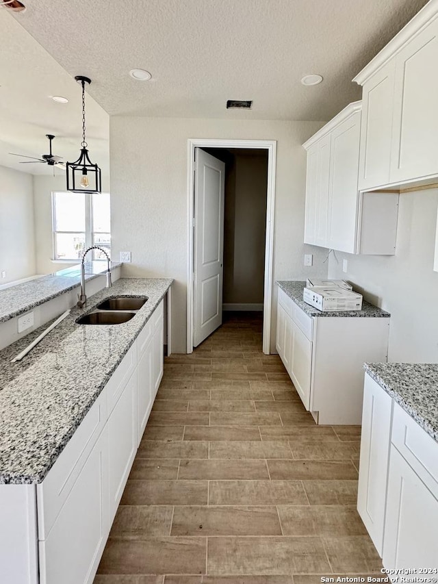 kitchen with a textured ceiling, sink, pendant lighting, light hardwood / wood-style flooring, and white cabinetry