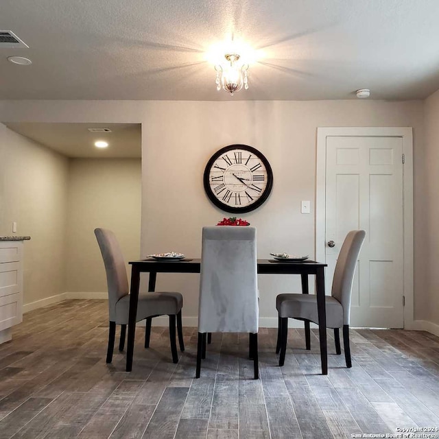 dining space with wood-type flooring, a textured ceiling, and a notable chandelier