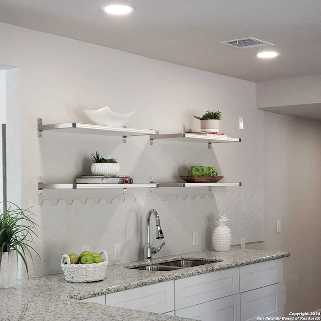 bar featuring light stone countertops, backsplash, white cabinetry, and sink