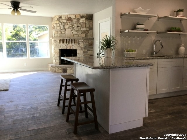 bar featuring ceiling fan, sink, dark wood-type flooring, dark stone counters, and white cabinets