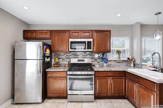 kitchen with sink, light tile patterned floors, appliances with stainless steel finishes, tasteful backsplash, and decorative light fixtures