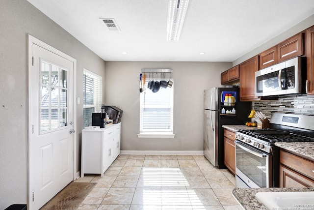 kitchen featuring decorative backsplash, light stone countertops, light tile patterned floors, and stainless steel appliances