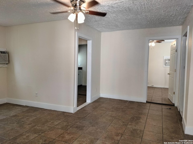 spare room featuring a wall mounted air conditioner, a textured ceiling, dark tile patterned flooring, and ceiling fan