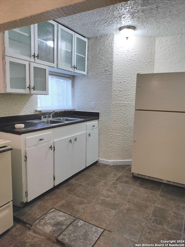 kitchen with stove, a textured ceiling, sink, white cabinets, and white fridge