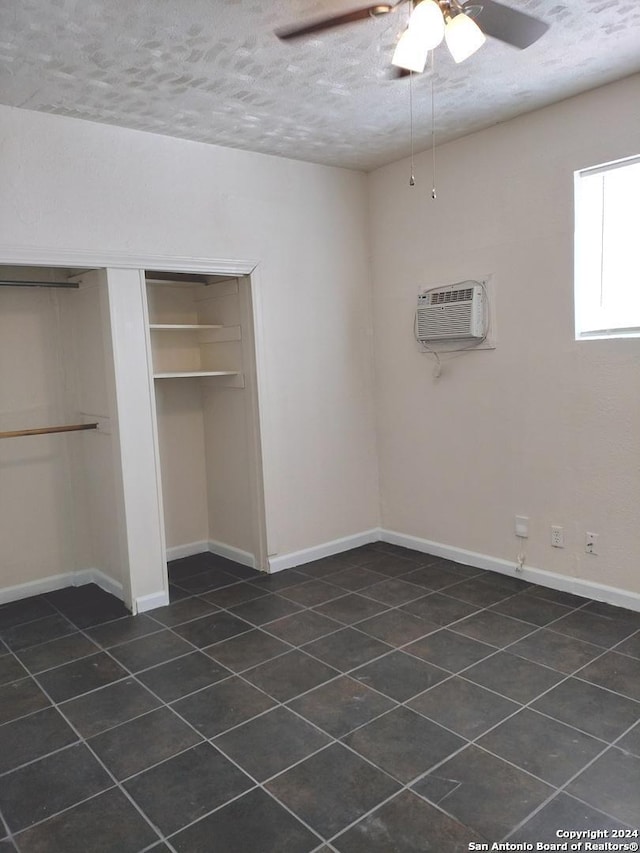 unfurnished bedroom featuring ceiling fan, dark tile patterned floors, a textured ceiling, a wall unit AC, and a closet