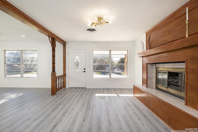 foyer entrance with a chandelier, light wood-type flooring, a wealth of natural light, and a tiled fireplace